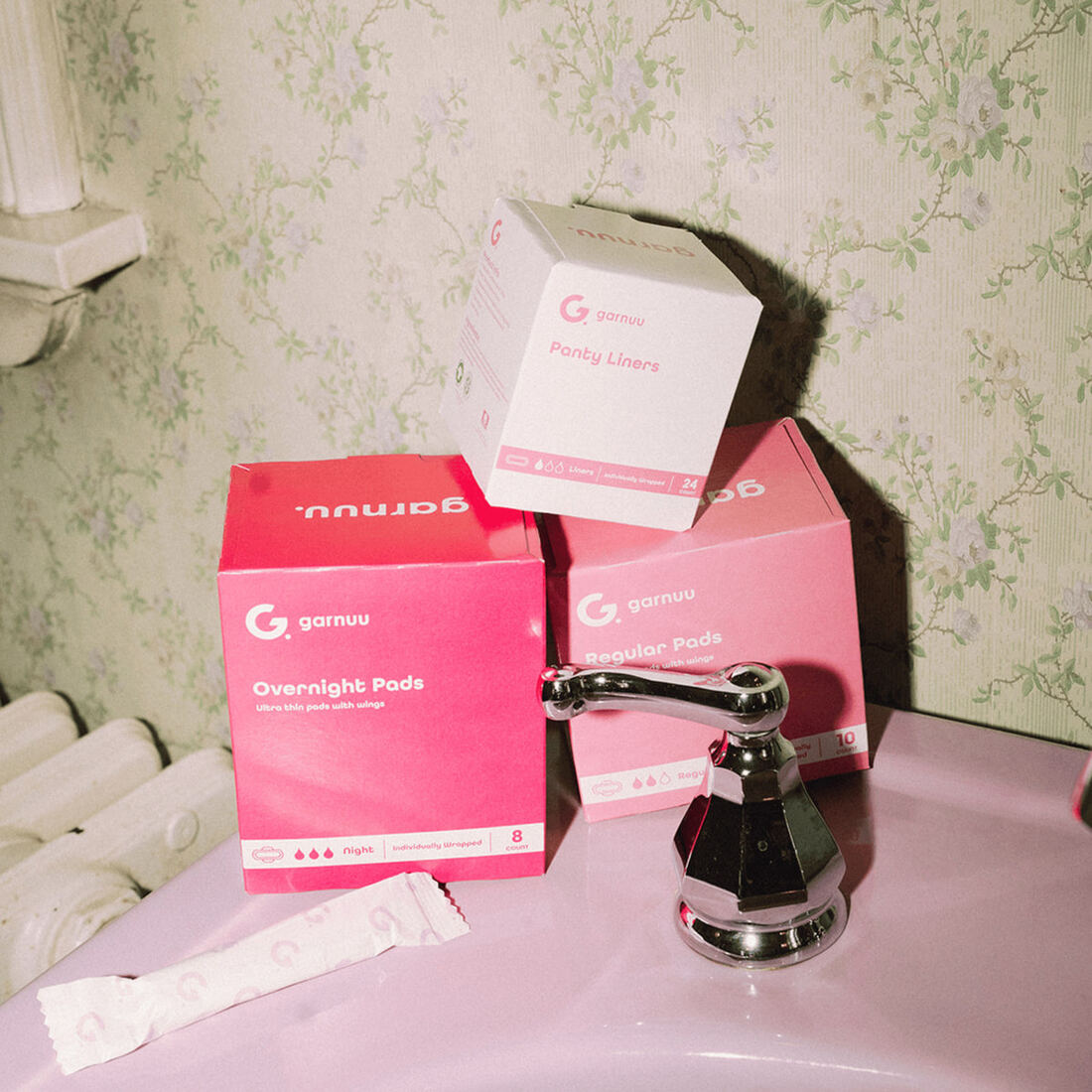 Three Garnuu boxes, overnight pads, regular pads and panty liners, stacked on a bathroom sink